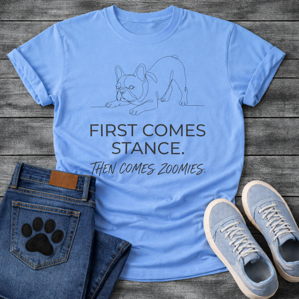 French Bulldog t-shirt with minimal continuous line art Frenchie in play bow zoomies stance, bold sans-serif text reading First Comes Stance Then Comes Zoomies, single dark ink on warm sand tee, premium clean design