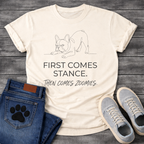 French Bulldog t-shirt with minimal continuous line art Frenchie in play bow zoomies stance, bold sans-serif text reading First Comes Stance Then Comes Zoomies, single dark ink on warm sand tee, premium clean design