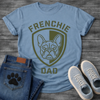 French Bulldog t-shirt with military style shield badge containing a geometric Frenchie face portrait, stencil font arched text reading Frenchie above and Dad below, single olive green ink graphic