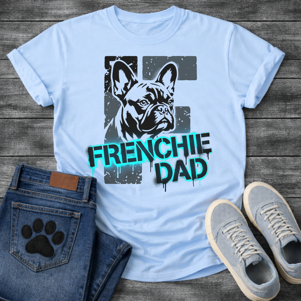 French Bulldog t-shirt with stencil-style Frenchie portrait over distressed dark block background, bold neon cyan graffiti text reading Frenchie Dad with black drip effects, high contrast urban street art graphic on warm sand tee
