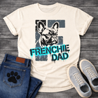 French Bulldog t-shirt with stencil-style Frenchie portrait over distressed dark block background, bold neon cyan graffiti text reading Frenchie Dad with black drip effects, high contrast urban street art graphic on warm sand tee
