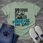 French Bulldog t-shirt with stencil-style Frenchie portrait over distressed dark block background, bold neon cyan graffiti text reading Frenchie Dad with black drip effects, high contrast urban street art graphic on warm sand tee
