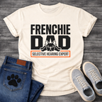 French Bulldog t-shirt with oversized bold typography reading Frenchie Dad, splooting Frenchie illustration tucked between the letters, orange bordered banner below reading Selective Hearing Expert, black and orange graphic design