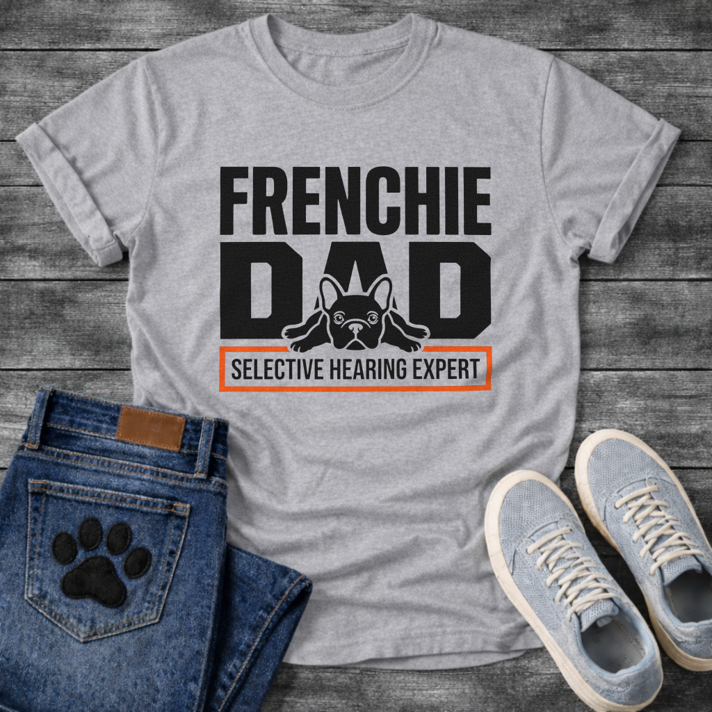 French Bulldog t-shirt with oversized bold typography reading Frenchie Dad, splooting Frenchie illustration tucked between the letters, orange bordered banner below reading Selective Hearing Expert, black and orange graphic design