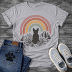 French Bulldog t-shirt with Frenchie silhouette seen from behind sitting among desert scrub plants and mesa rock formations, large boho rainbow arch above in muted pink terracotta gold and sage tones, distressed vintage texture, no text
