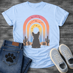 French Bulldog t-shirt with Frenchie silhouette seen from behind sitting in a desert landscape, framed by a gradient rainbow arch in pink orange yellow and blue tones, constellation star patterns above, cactus silhouettes on either side, painterly boho illustration graphic