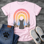 French Bulldog t-shirt with Frenchie silhouette seen from behind sitting in a desert landscape, framed by a gradient rainbow arch in pink orange yellow and blue tones, constellation star patterns above, cactus silhouettes on either side, painterly boho illustration graphic
