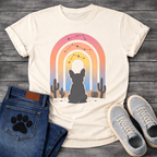 French Bulldog t-shirt with Frenchie silhouette seen from behind sitting in a desert landscape, framed by a gradient rainbow arch in pink orange yellow and blue tones, constellation star patterns above, cactus silhouettes on either side, painterly boho illustration graphic