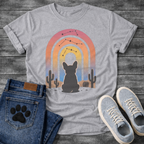 French Bulldog t-shirt with Frenchie silhouette seen from behind sitting in a desert landscape, framed by a gradient rainbow arch in pink orange yellow and blue tones, constellation star patterns above, cactus silhouettes on either side, painterly boho illustration graphic