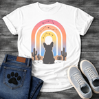 French Bulldog t-shirt with Frenchie silhouette seen from behind sitting in a desert landscape, framed by a gradient rainbow arch in pink orange yellow and blue tones, constellation star patterns above, cactus silhouettes on either side, painterly boho illustration graphic