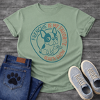 French Bulldog t-shirt with circular badge design, cartoon Frenchie holding a TV remote, teal and coral circular text reading Frenchie Is My Favorite Reality Show, two-color retro emblem on warm sand tee