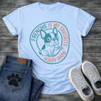 French Bulldog t-shirt with circular badge design, cartoon Frenchie holding a TV remote, teal and coral circular text reading Frenchie Is My Favorite Reality Show, two-color retro emblem on warm sand tee