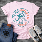 French Bulldog t-shirt with circular badge design, cartoon Frenchie holding a TV remote, teal and coral circular text reading Frenchie Is My Favorite Reality Show, two-color retro emblem on warm sand tee
