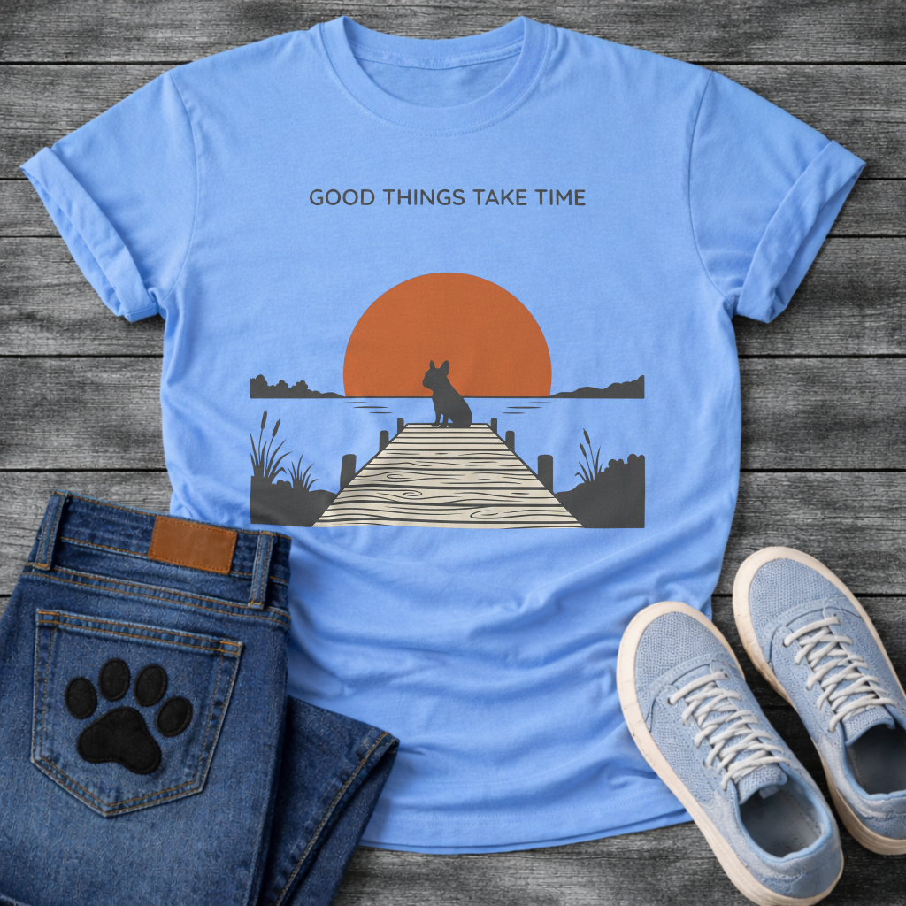 French Bulldog t-shirt with Frenchie silhouette sitting on a wooden dock facing a large terracotta sunset over water, reeds and shoreline on either side, text above reading Good Things Take Time, two-color vintage landscape illustration