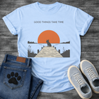 French Bulldog t-shirt with Frenchie silhouette sitting on a wooden dock facing a large terracotta sunset over water, reeds and shoreline on either side, text above reading Good Things Take Time, two-color vintage landscape illustration