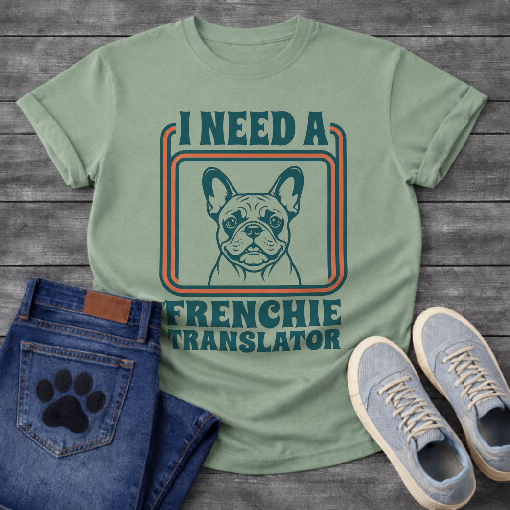 French Bulldog t-shirt with retro 70s groovy typography reading I Need a Frenchie Translator, detailed Frenchie portrait centered in teal and orange rounded rectangle frame, two-color retro illustration on warm sand tee