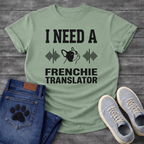 French Bulldog t-shirt with bold collegiate typography reading I Need a Frenchie Translator, black Frenchie face silhouette flanked by sound wave graphics, single dark ink on warm sand tee, clean graphic design