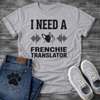 French Bulldog t-shirt with bold collegiate typography reading I Need a Frenchie Translator, black Frenchie face silhouette flanked by sound wave graphics, single dark ink on warm sand tee, clean graphic design