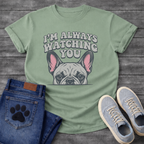 French Bulldog t-shirt with retro 70s bubble typography reading I'm Always Watching You above a peeking Frenchie face with pink inner ears, vintage halftone illustration on warm sand tee, groovy retro style