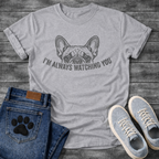 French Bulldog t-shirt with vintage halftone Frenchie face peeking over distressed arched text reading I'm Always Watching You, dark single-ink illustration on warm sand tee, retro graphic style