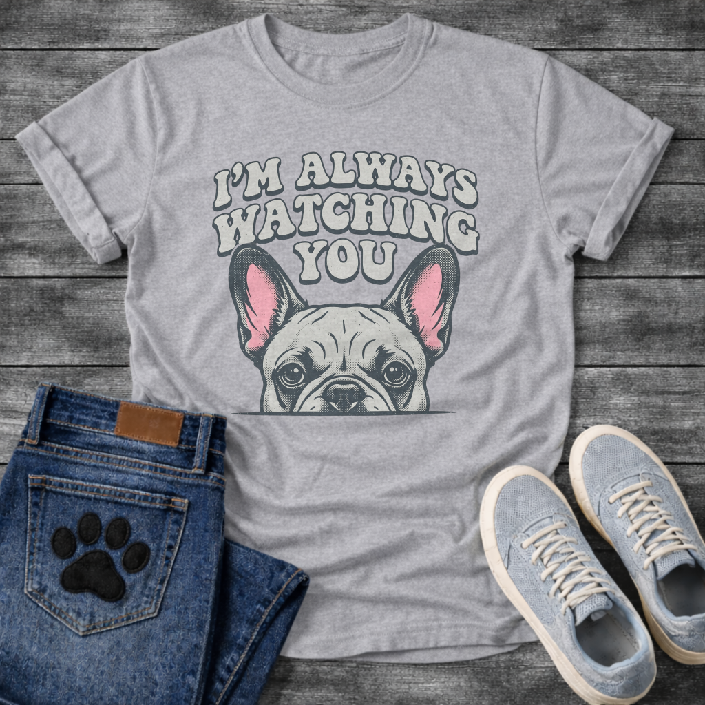 French Bulldog t-shirt with retro 70s bubble typography reading I'm Always Watching You above a peeking Frenchie face with pink inner ears, vintage halftone illustration on warm sand tee, groovy retro style