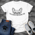 French Bulldog t-shirt with vintage halftone Frenchie face peeking over distressed arched text reading I'm Always Watching You, dark single-ink illustration on warm sand tee, retro graphic style