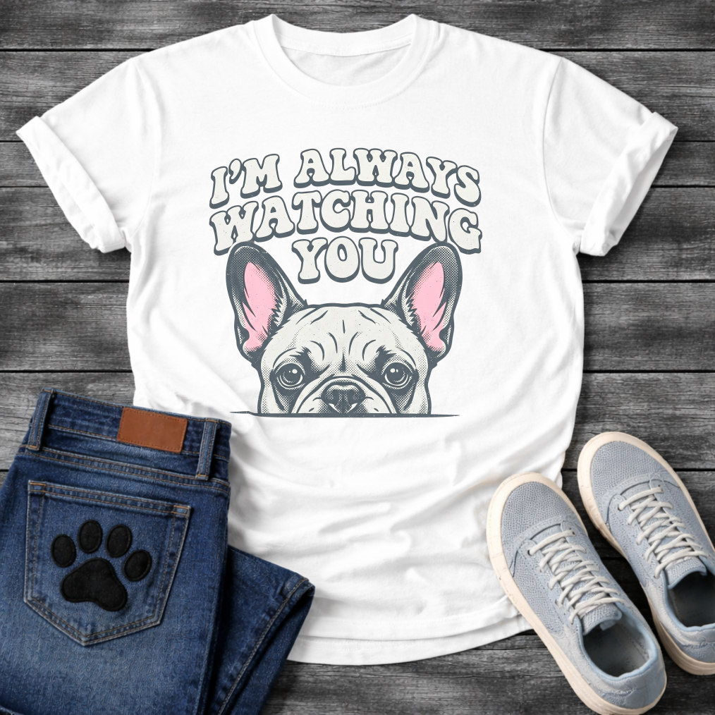 French Bulldog t-shirt with retro 70s bubble typography reading I'm Always Watching You above a peeking Frenchie face with pink inner ears, vintage halftone illustration on warm sand tee, groovy retro style