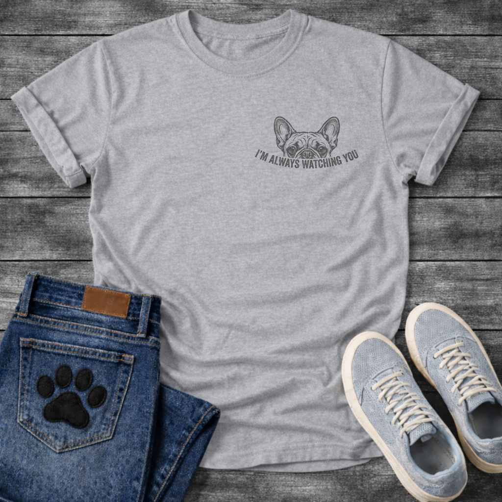 French Bulldog left chest pocket t-shirt with vintage halftone Frenchie face peeking over distressed arched text reading I'm Always Watching You, small dark single-ink graphic on warm sand tee, retro pocket print style
