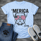 French Bulldog t-shirt with bold 'Merica text above a detailed Frenchie face wearing American flag aviator sunglasses, 1776 text bottom right, black and red patriotic graphic on warm sand tee