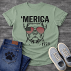 French Bulldog t-shirt with bold 'Merica text above a detailed Frenchie face wearing American flag aviator sunglasses, 1776 text bottom right, black and red patriotic graphic on warm sand tee