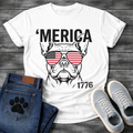 French Bulldog t-shirt with bold 'Merica text above a detailed Frenchie face wearing American flag aviator sunglasses, 1776 text bottom right, black and red patriotic graphic on warm sand tee