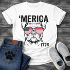 French Bulldog t-shirt with bold 'Merica text above a detailed Frenchie face wearing American flag aviator sunglasses, 1776 text bottom right, black and red patriotic graphic on warm sand tee