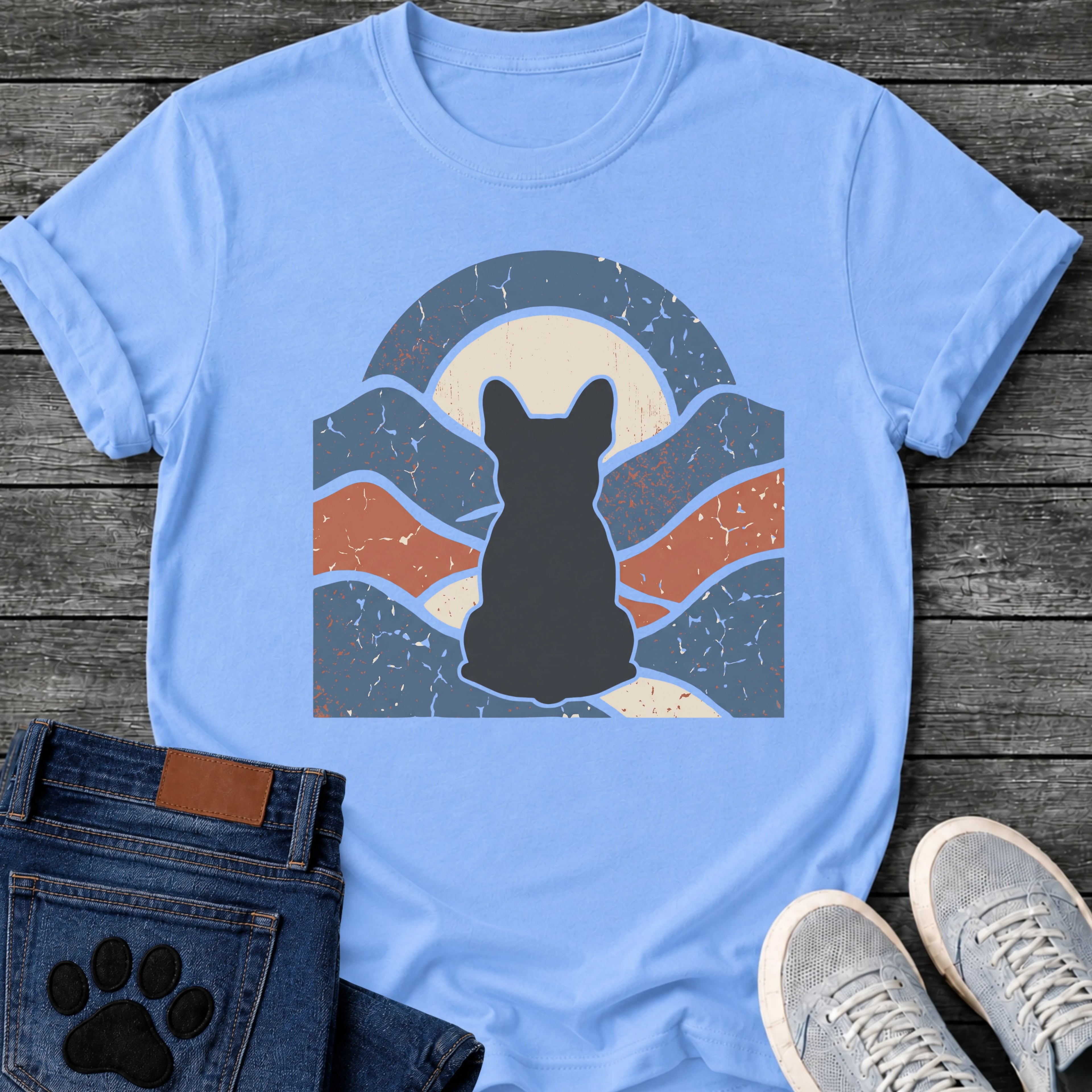 French Bulldog t-shirt with Frenchie silhouette seen from behind centered in a wavy layered landscape of slate blue and terracotta, cream moon rising behind the head, arched frame above, heavy crackle distressed texture throughout, no text earthy art graphic