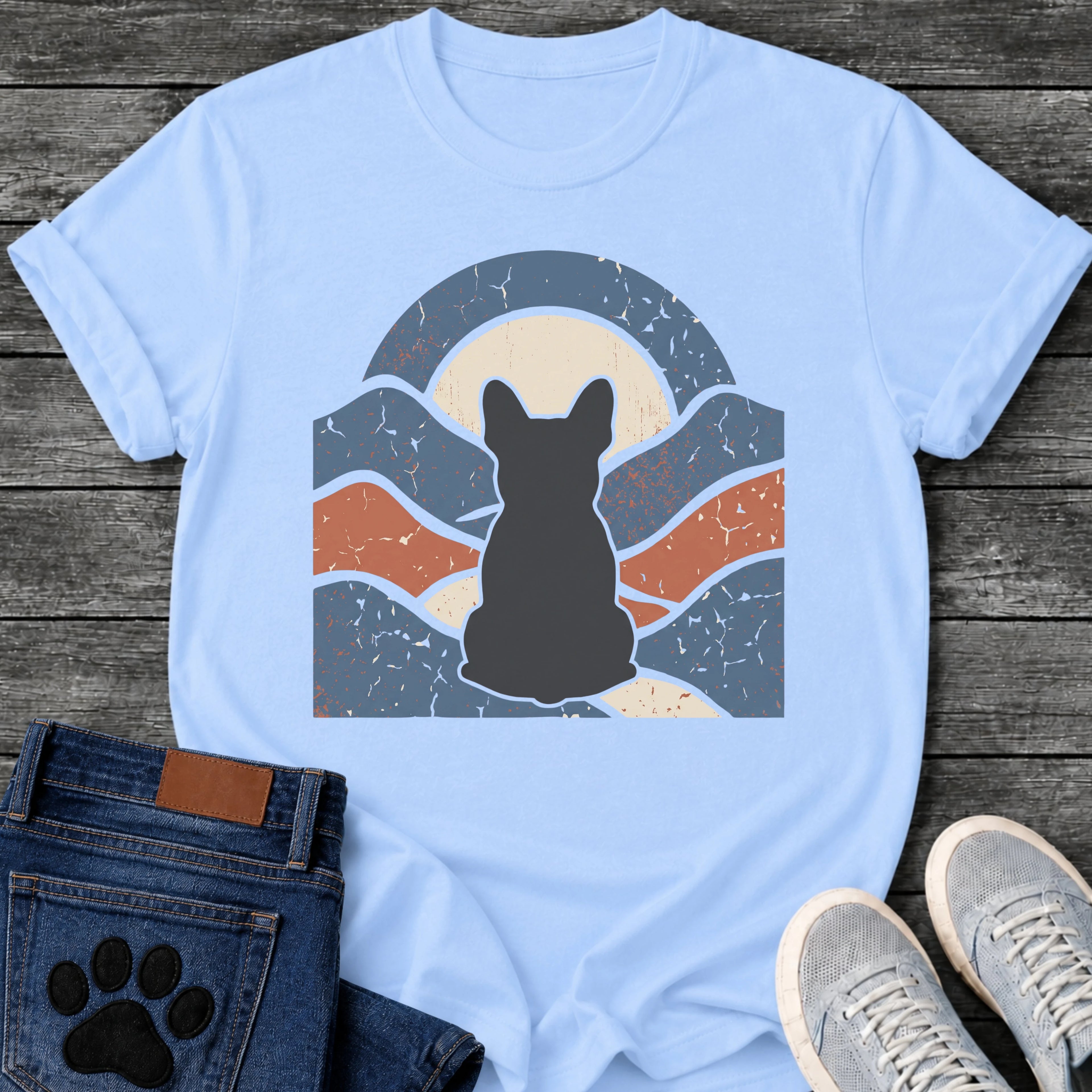 French Bulldog t-shirt with Frenchie silhouette seen from behind centered in a wavy layered landscape of slate blue and terracotta, cream moon rising behind the head, arched frame above, heavy crackle distressed texture throughout, no text earthy art graphic