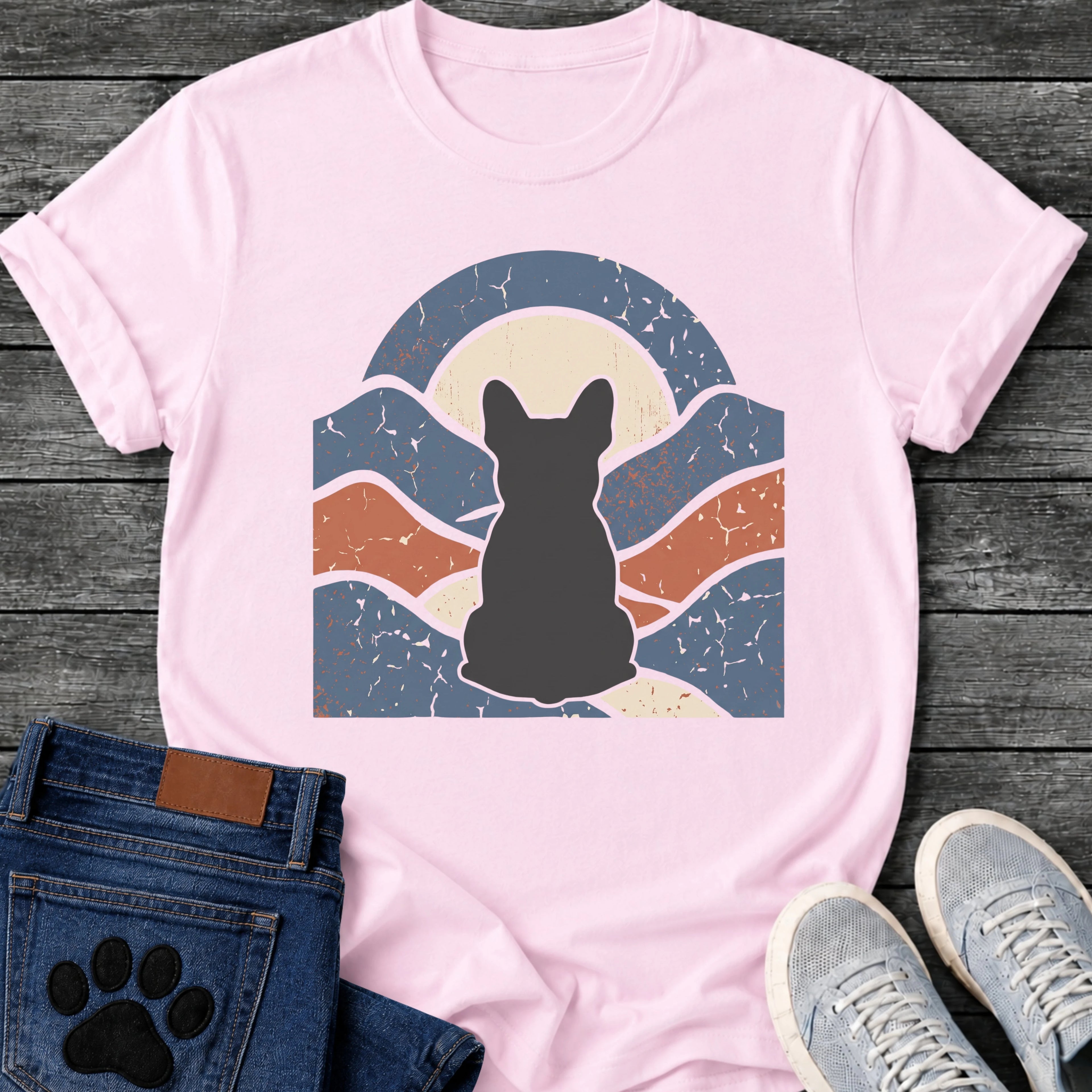French Bulldog t-shirt with Frenchie silhouette seen from behind centered in a wavy layered landscape of slate blue and terracotta, cream moon rising behind the head, arched frame above, heavy crackle distressed texture throughout, no text earthy art graphic