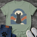 French Bulldog t-shirt with Frenchie silhouette seen from behind centered in a wavy layered landscape of slate blue and terracotta, cream moon rising behind the head, arched frame above, heavy crackle distressed texture throughout, no text earthy art graphic