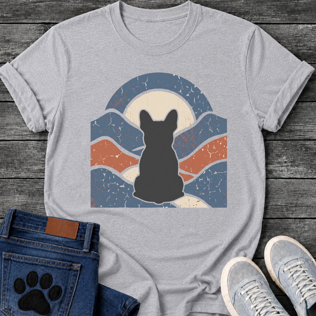French Bulldog t-shirt with Frenchie silhouette seen from behind centered in a wavy layered landscape of slate blue and terracotta, cream moon rising behind the head, arched frame above, heavy crackle distressed texture throughout, no text earthy art graphic