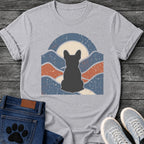 French Bulldog t-shirt with Frenchie silhouette seen from behind centered in a wavy layered landscape of slate blue and terracotta, cream moon rising behind the head, arched frame above, heavy crackle distressed texture throughout, no text earthy art graphic