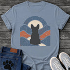 French Bulldog t-shirt with Frenchie silhouette seen from behind centered in a wavy layered landscape of slate blue and terracotta, cream moon rising behind the head, arched frame above, heavy crackle distressed texture throughout, no text earthy art graphic