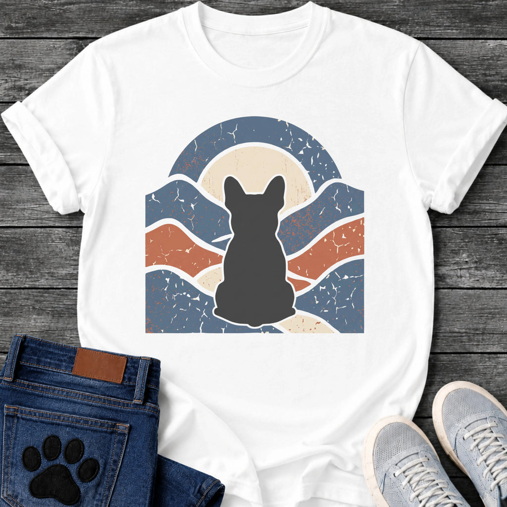 French Bulldog t-shirt with Frenchie silhouette seen from behind centered in a wavy layered landscape of slate blue and terracotta, cream moon rising behind the head, arched frame above, heavy crackle distressed texture throughout, no text earthy art graphic