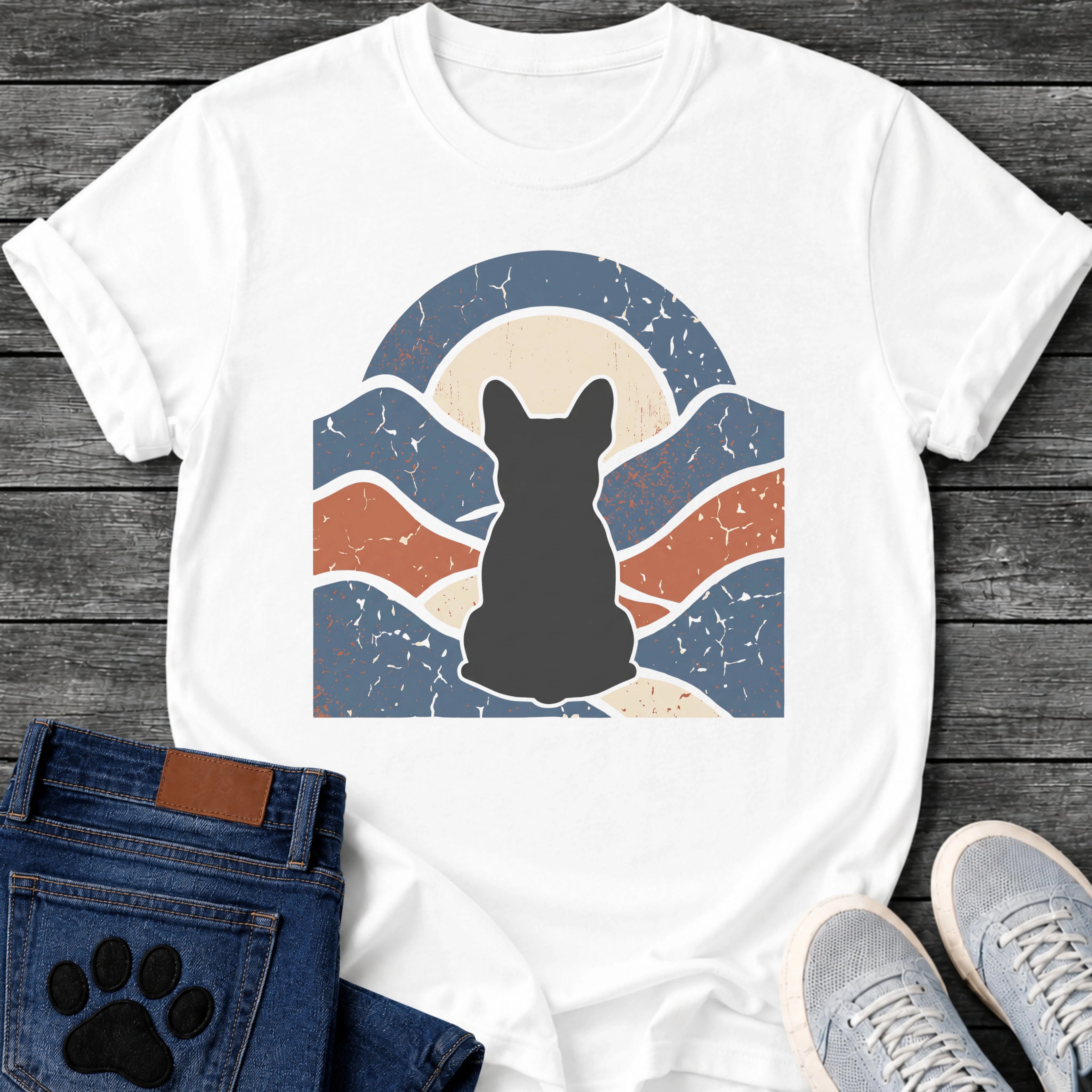 French Bulldog t-shirt with Frenchie silhouette seen from behind centered in a wavy layered landscape of slate blue and terracotta, cream moon rising behind the head, arched frame above, heavy crackle distressed texture throughout, no text earthy art graphic