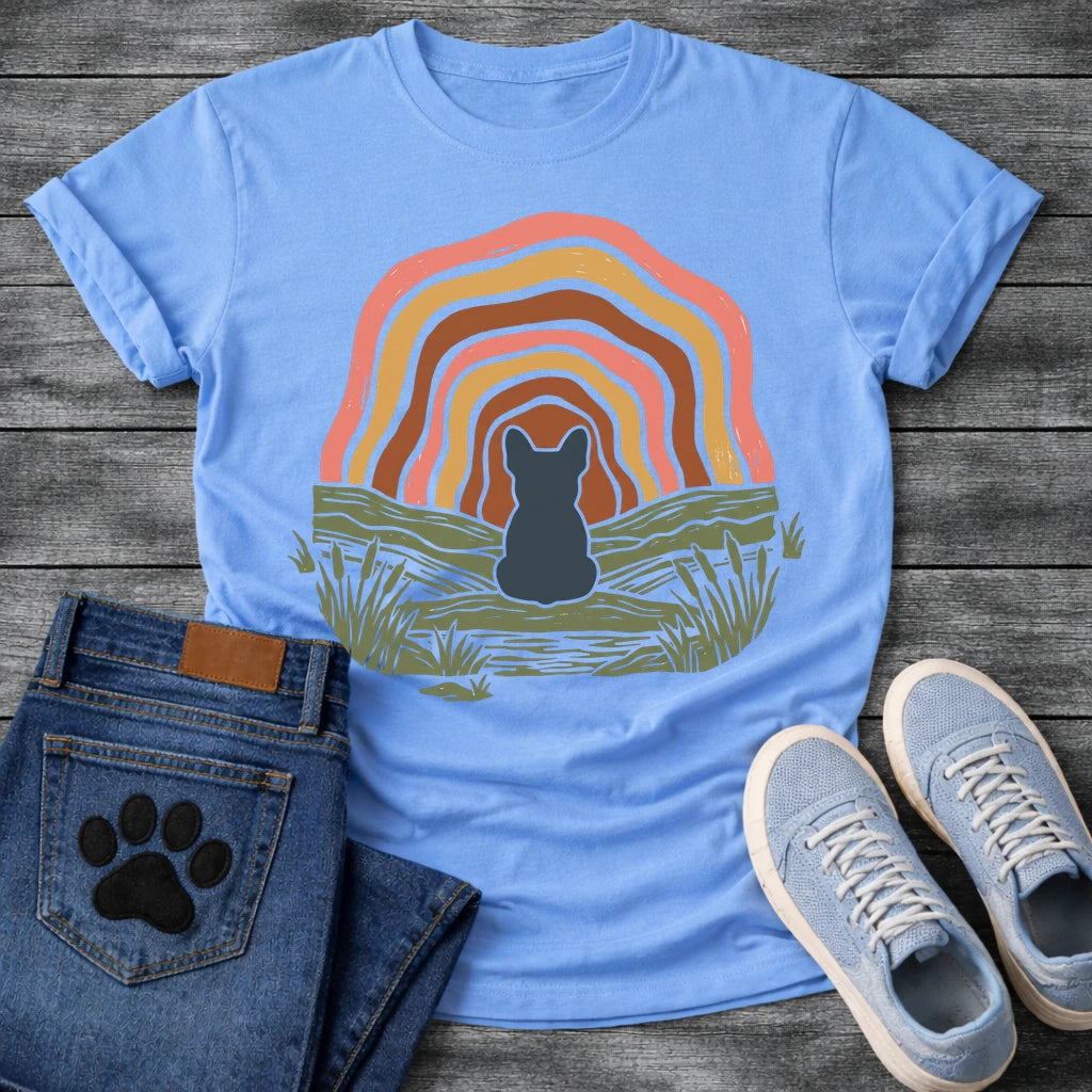 French Bulldog t-shirt with Frenchie silhouette seen from behind sitting on a textured grassy bank, layered concentric organic arch in blush pink gold and warm brown framing the scene, reed and grass detail, no text boho art graphic