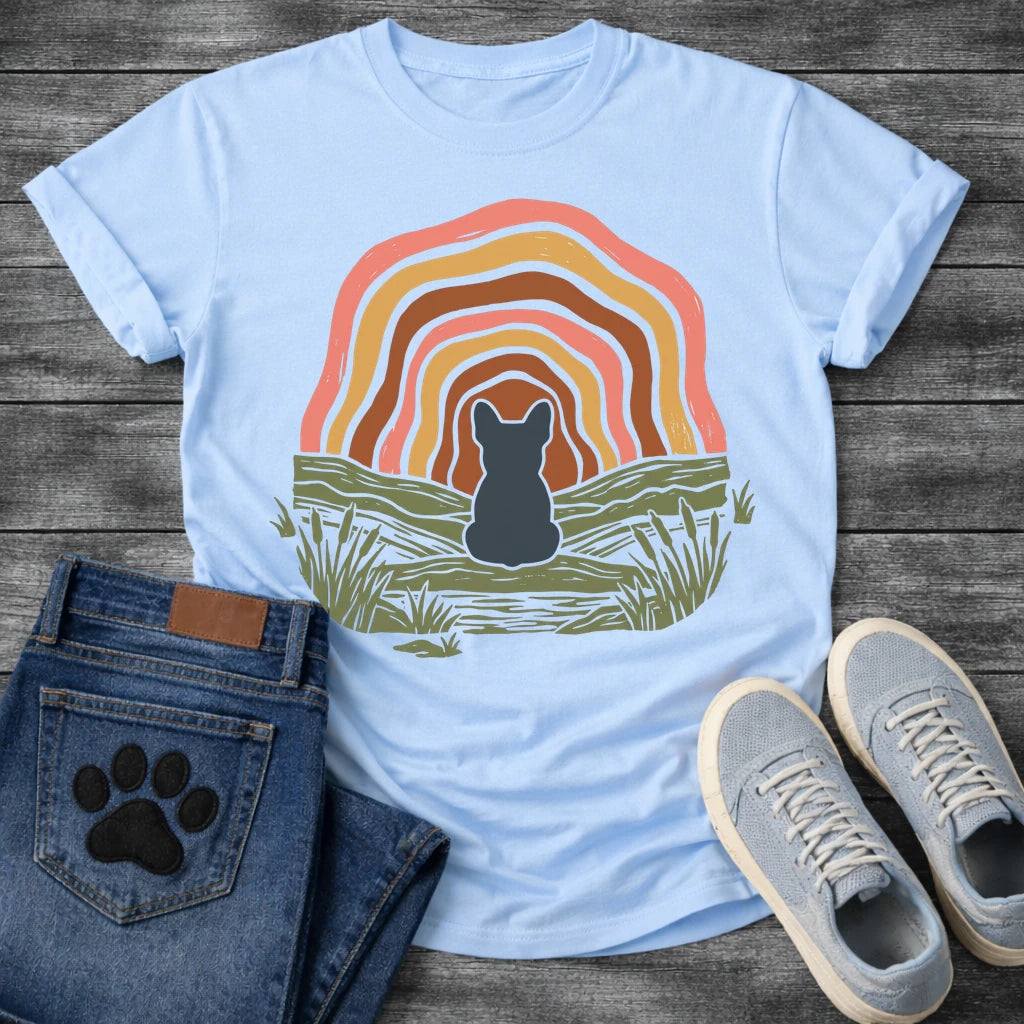 French Bulldog t-shirt with Frenchie silhouette seen from behind sitting on a textured grassy bank, layered concentric organic arch in blush pink gold and warm brown framing the scene, reed and grass detail, no text boho art graphic