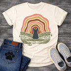 French Bulldog t-shirt with Frenchie silhouette seen from behind sitting on a textured grassy bank, layered concentric organic arch in blush pink gold and warm brown framing the scene, reed and grass detail, no text boho art graphic