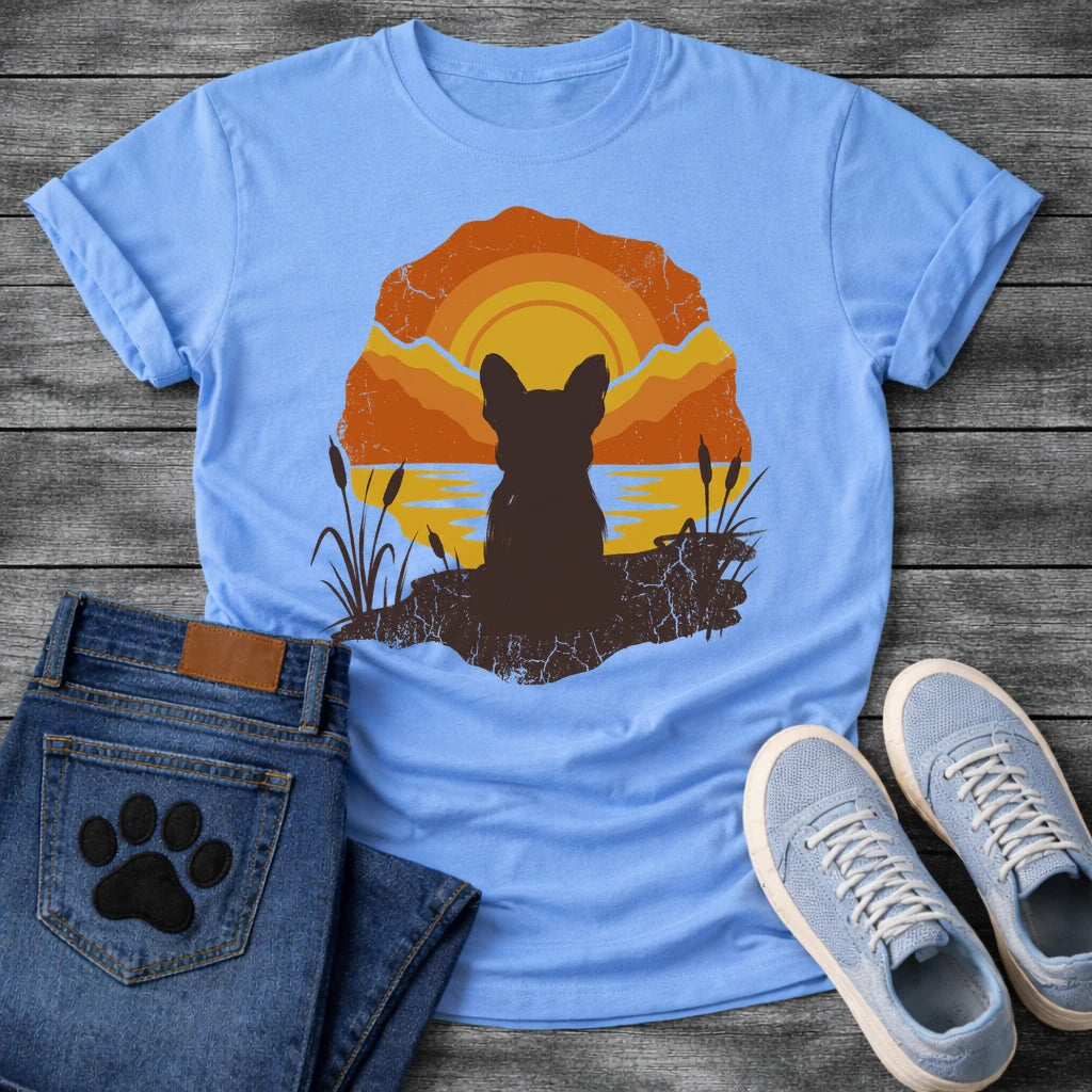 French Bulldog t-shirt with Frenchie silhouette seen from behind sitting on cracked earth beside water, cattail reeds on either side, bold concentric sun rings in deep orange and gold behind, distressed vintage texture throughout, organic blob frame, no text
