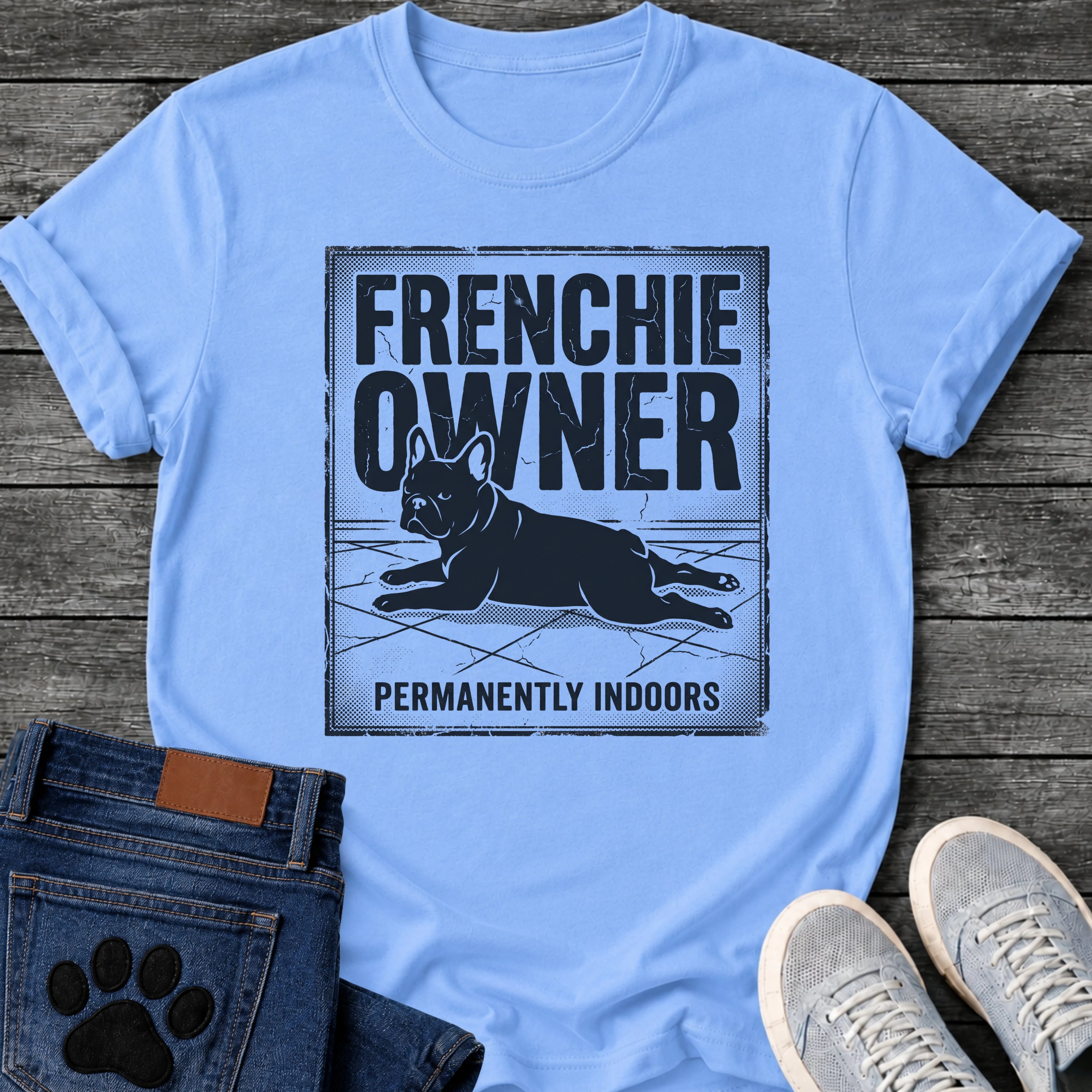 French Bulldog t-shirt with vintage distressed poster frame, bold oversized text reading Frenchie Owner above a splooting Frenchie lying flat on tile floor, bold banner text below reading Permanently Indoors, single dark ink halftone graphic with heavy crackle texture