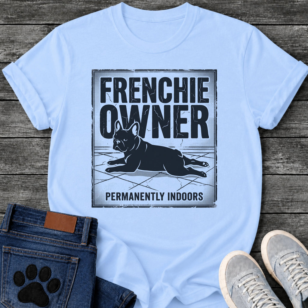 French Bulldog t-shirt with vintage distressed poster frame, bold oversized text reading Frenchie Owner above a splooting Frenchie lying flat on tile floor, bold banner text below reading Permanently Indoors, single dark ink halftone graphic with heavy crackle texture