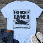 French Bulldog t-shirt with vintage distressed poster frame, bold oversized text reading Frenchie Owner above a splooting Frenchie lying flat on tile floor, bold banner text below reading Permanently Indoors, single dark ink halftone graphic with heavy crackle texture