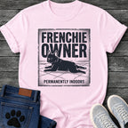 French Bulldog t-shirt with vintage distressed poster frame, bold oversized text reading Frenchie Owner above a splooting Frenchie lying flat on tile floor, bold banner text below reading Permanently Indoors, single dark ink halftone graphic with heavy crackle texture