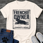 French Bulldog t-shirt with vintage distressed poster frame, bold oversized text reading Frenchie Owner above a splooting Frenchie lying flat on tile floor, bold banner text below reading Permanently Indoors, single dark ink halftone graphic with heavy crackle texture